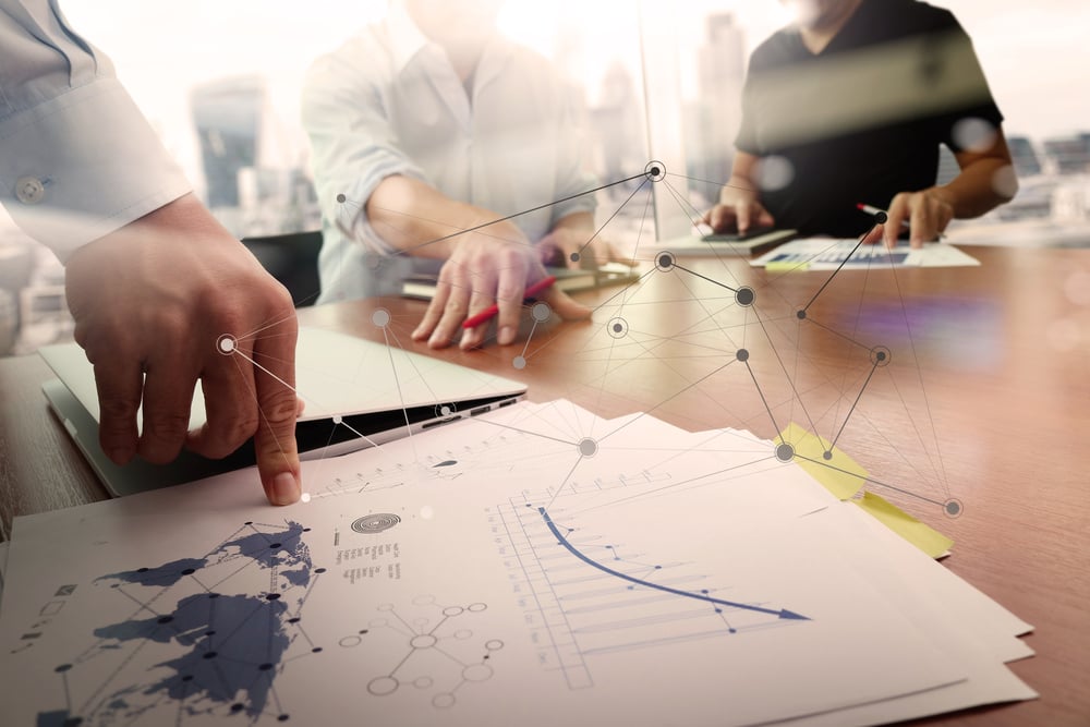 Business documents on office table with smart phone and laptop computer and graph financial with social network diagram and two colleagues discussing data in the background